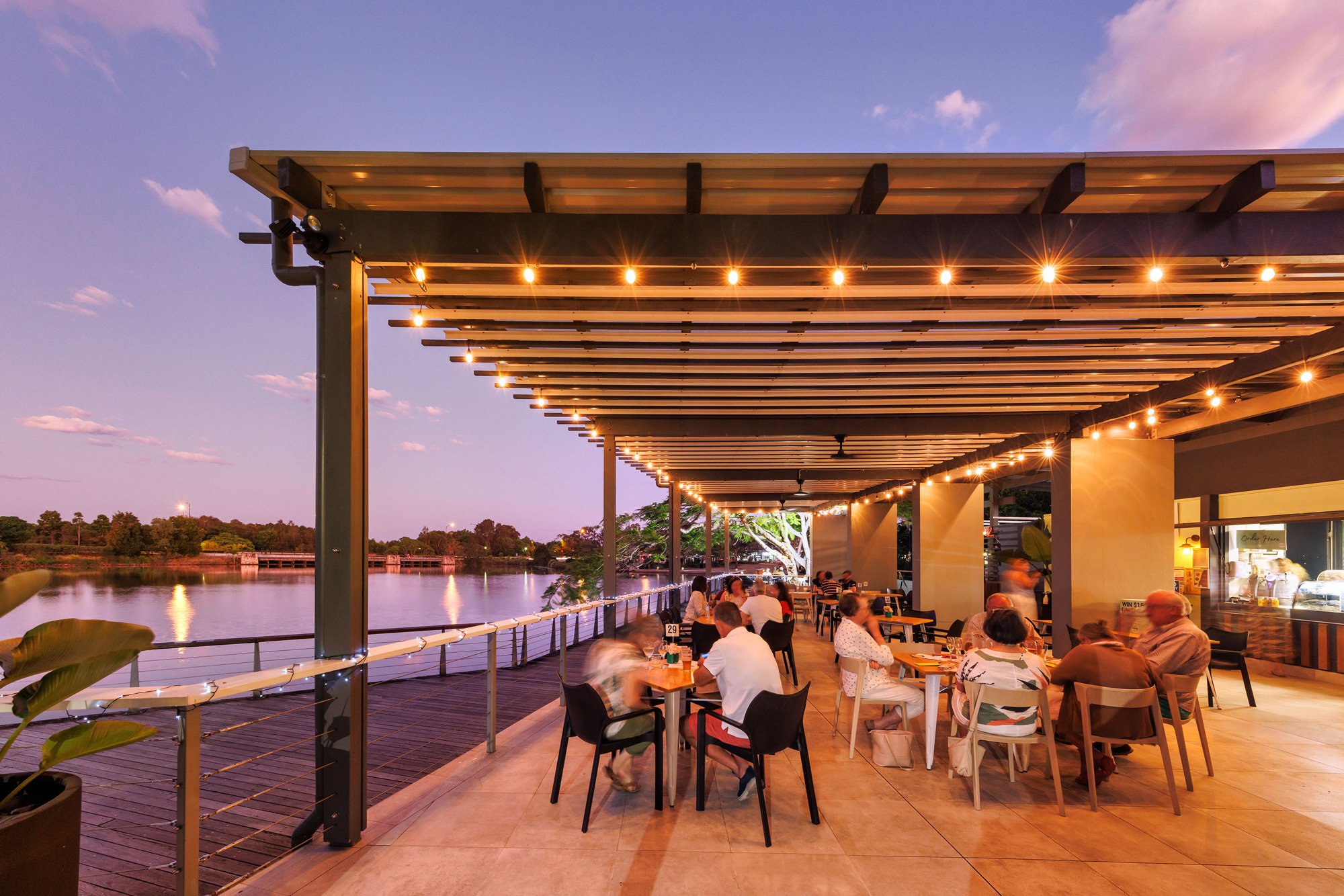 Waterside deck at dusk under a pergola with festoon and pendant lighting