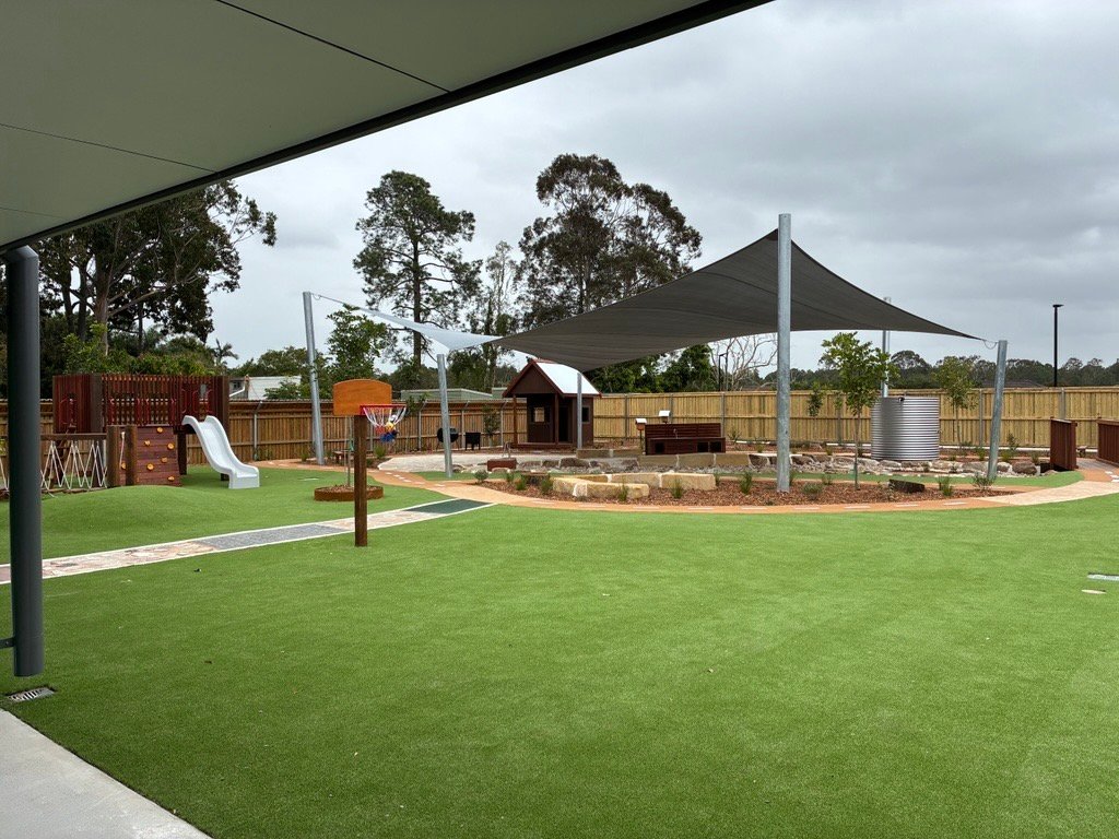 Outdoor play area with synthetic turf, shade sail and play equipment