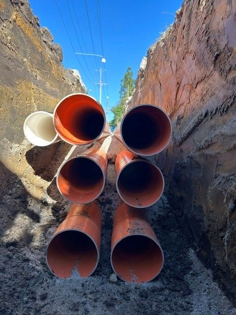 Stacked orange conduits in a deep trench with power poles beyond