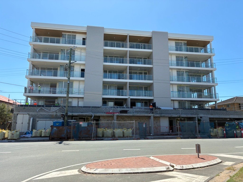 Five-storey residential apartment building with glass balconies, seen from the street