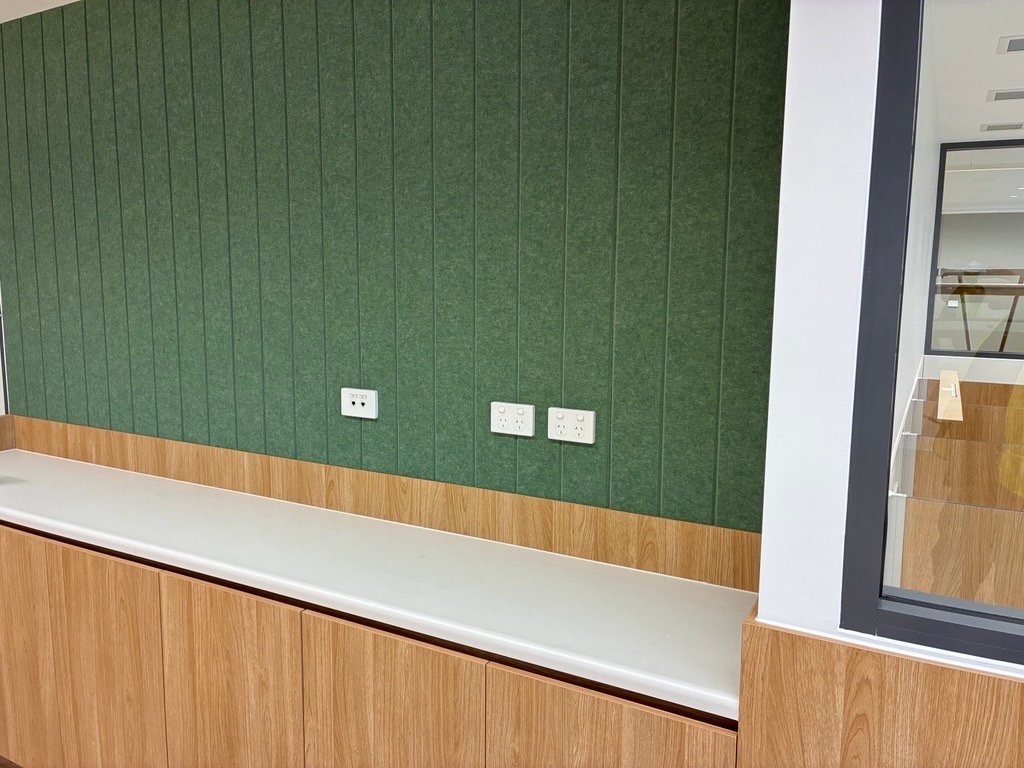 Green acoustic feature wall above a timber bench with power points